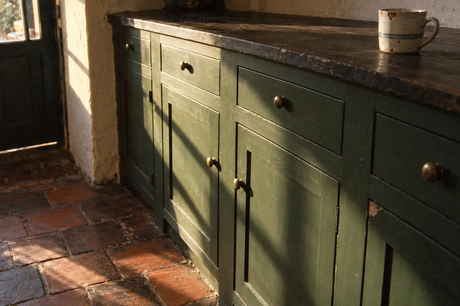 Green painted inset cabinets with brass knobs, the doors and drawers sitting flush inside the face frame beneath a worn dark wood top