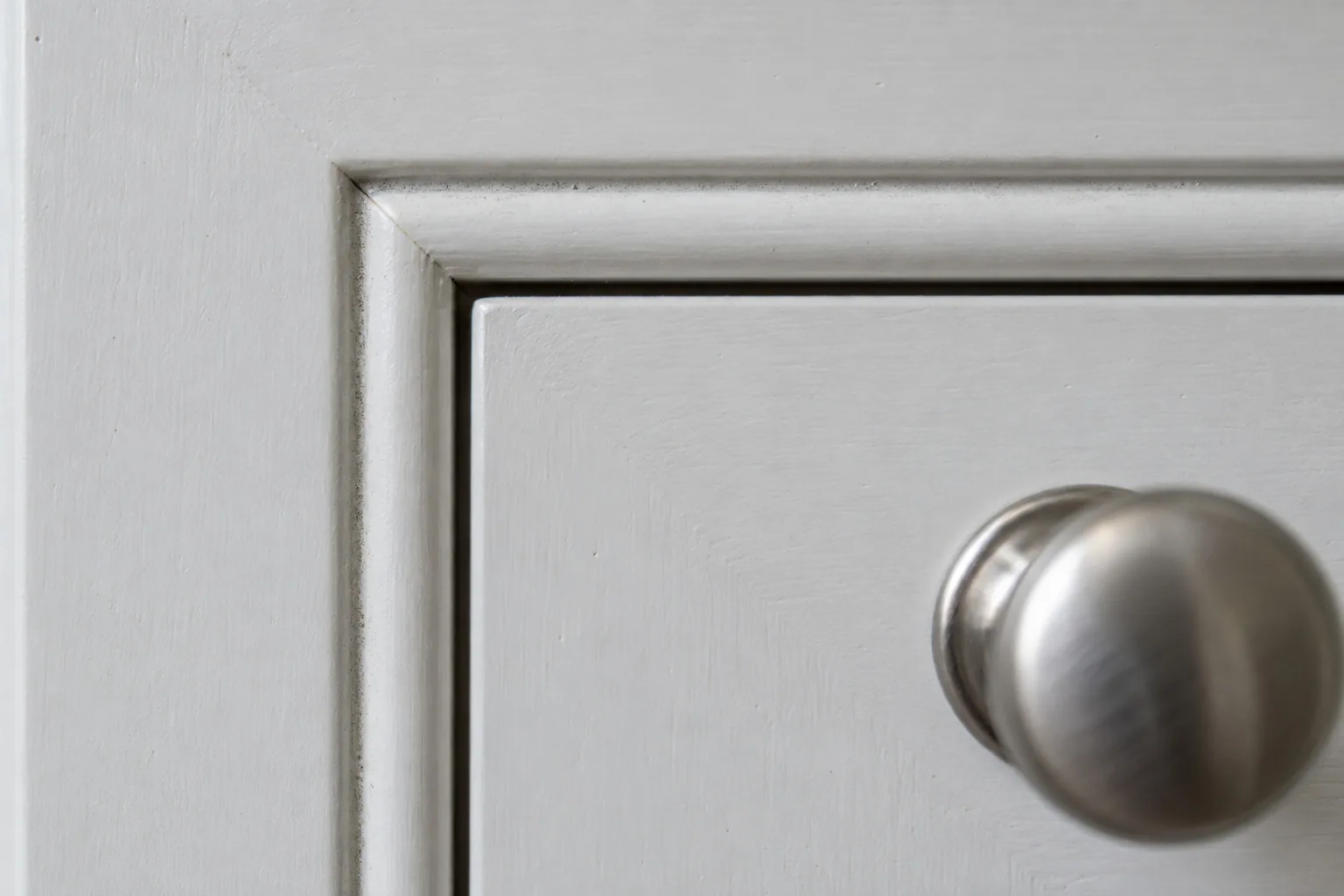 Close-up of a white beaded inset drawer, with a thin bead of molding tracing the face-frame opening and a brushed nickel knob