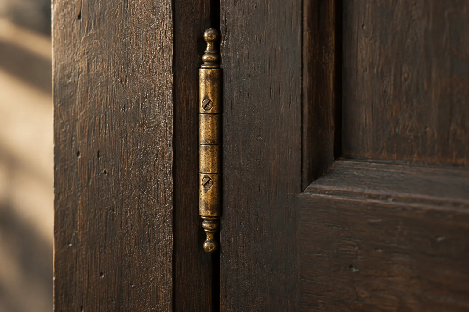 Close-up of an aged brass finial hinge on a dark stained wood inset cabinet door